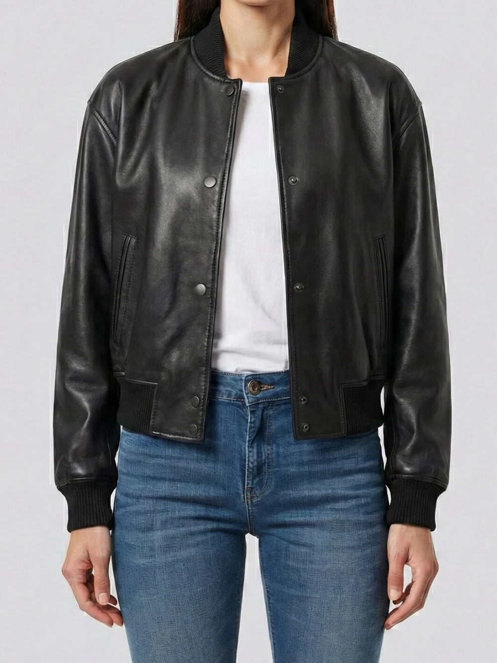 Person wearing a black leather jacket over a white shirt and blue jeans on a plain background