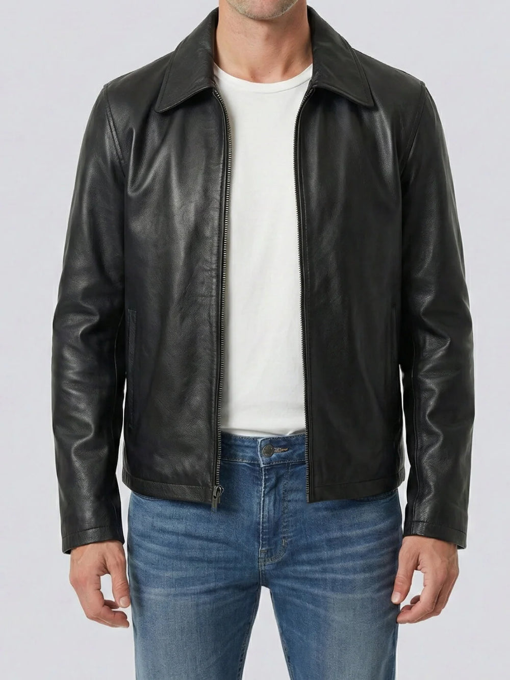 Man wearing a black leather jacket over a white shirt and blue jeans on a light gray background