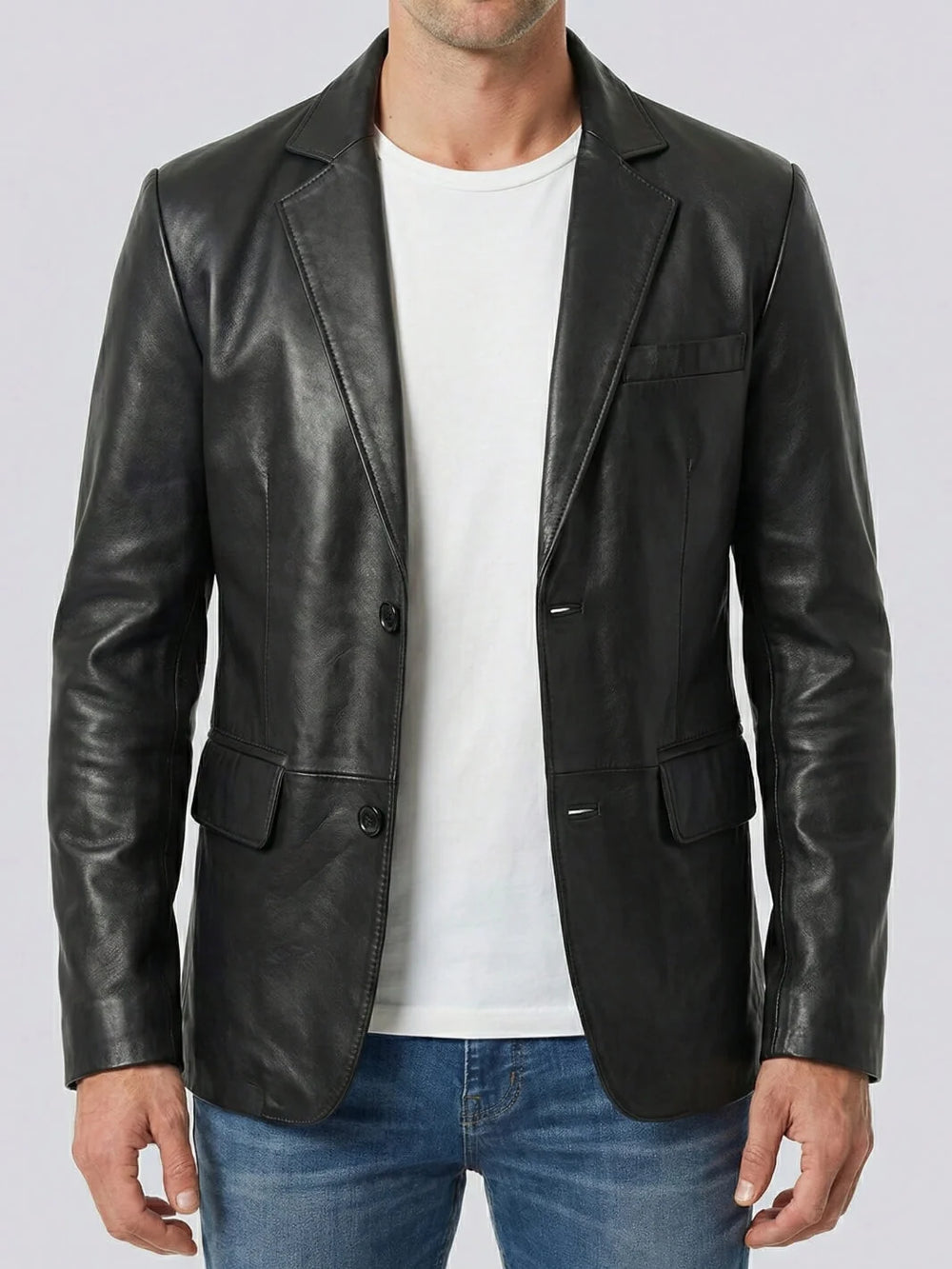 Man wearing a black leather blazer over a white shirt and blue jeans on a light gray background